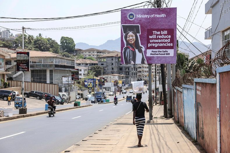ARCHIVO - Una mujer pasa junto a un cartel que promociona el proyecto de ley de Maternidad Segura, en Wilkinson Road, Freetown, Sierra Leone, el 12 de marzo de 2025. (AP Foto/Caitlin Kelly, archivo)
