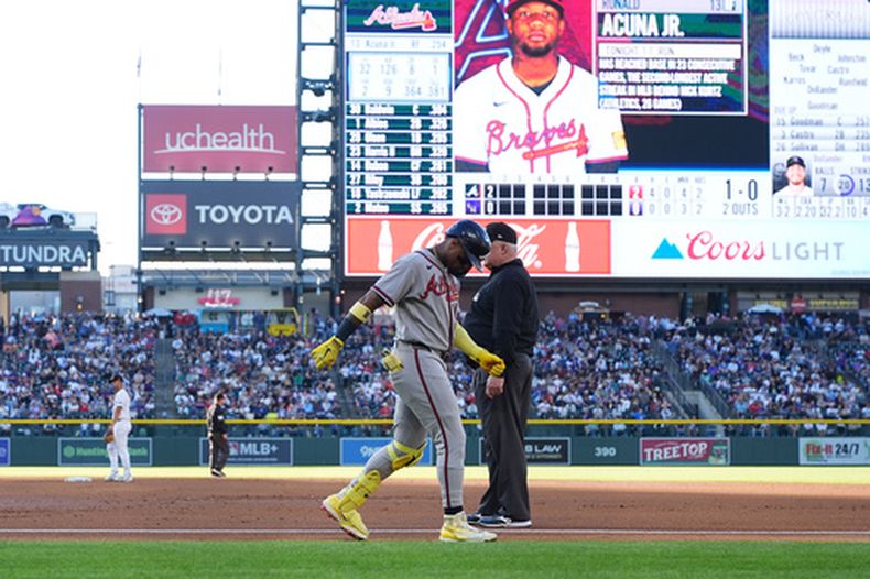 Ronald Acuña Jr. (centro izquierda), de los Bravos de Atlanta, camina con dificultad tras lesionarse mientras corría tras un roletazo, mientras el umpire de primera base Bill Miller (centro derecha) observa durante la segunda entrada de un partido de béisbol contra los Rockies de Colorado, el sábado 2 de mayo de 2026, en Denver. (AP Foto/David Zalubowski)