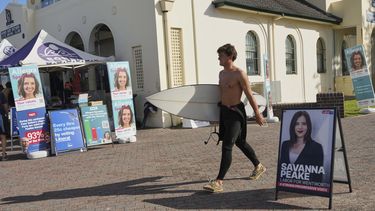 Un surfista pasa con su tabla por delante de un puesto de votación en Bondi Beach, Sydney, el 3 de mayo de 2025. (AP Foto/Mark Baker)