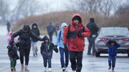 Migrantes corren bajo la lluvia hacia las carpas instaladas en el antiguo aeropuerto Floyd Bennett Field, el martes 9 de enero de 2024, en el distrito de Brooklyn en Nueva York. (AP Foto/Mary Altaffer)