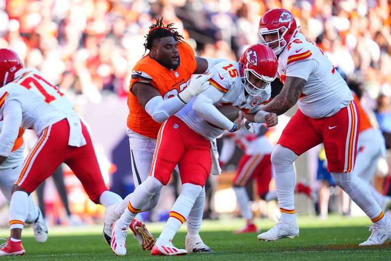 Malcolm Roach, izquierda, tackle defensivo de los Broncos de Denver, pierde el casco mientras persigue y sujeta a Patrick Mahomes (15), quarterback de los Chiefs de Kansas City, durante la primera mitad del partido de la NFL del domingo 16 de noviembre de 2025, en Denver. (AP Foto/Jack Dempsey)