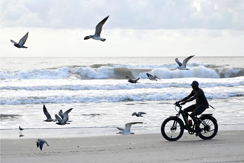Un ciclista recorre la playa junto a gaviotas mientras la tormenta tropical Imelda agita las olas, el lunes 29 de septiembre de 2025, en Cocoa Beach, Florida. (AP Foto/Phelan M. Ebenhack)