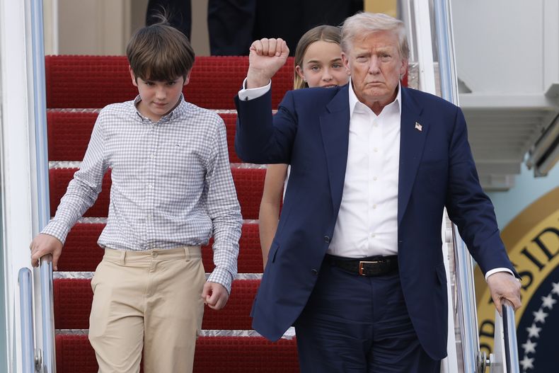 El presidente estadounidense Donald Trump alza un puño al bajar del Air Force One con sus nietos, Spencer y Chloe, a su llegada a la Base Conjunta Andrews, el 29 de julio de 2025, en Maryland. (AP Foto/Luis M. Alvarez)