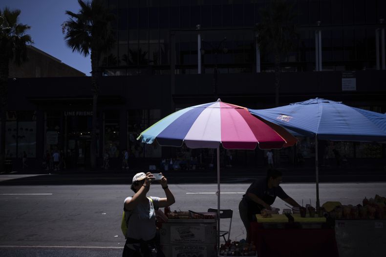 Una persona toma fotos del teatro chino mientras un vendedor callejero trabaja cerca de la sección de Hollywood en Los Ángeles, el martes 19 de agosto de 2025. (AP Foto/Jae C. Hong)