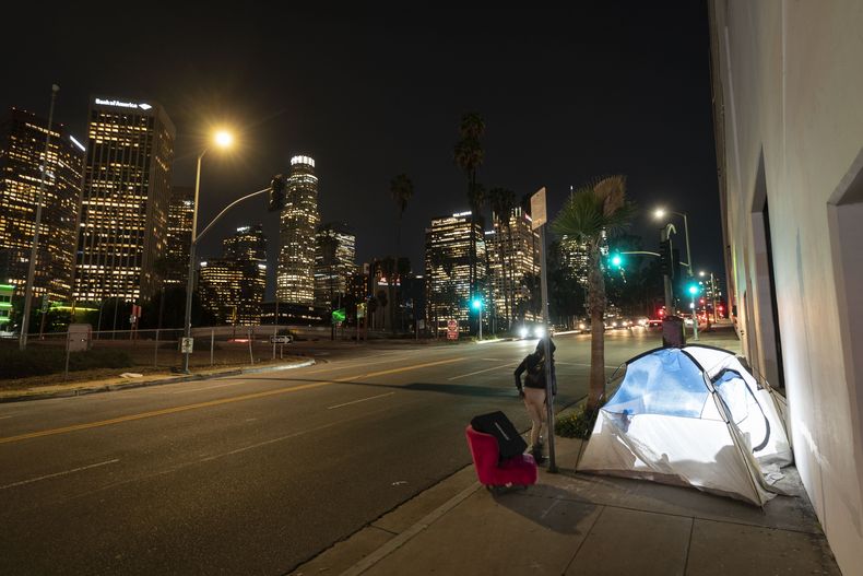 ARCHIVO - En esta imagen, iluminada por un flash externo, una mujer pasa por delante de una tienda de campaña de una persona sin hogar con una silla, en el centro de Los Ángeles, el 16 de febrero de 2023. (AP Foto/Jae C. Hong, archivo)