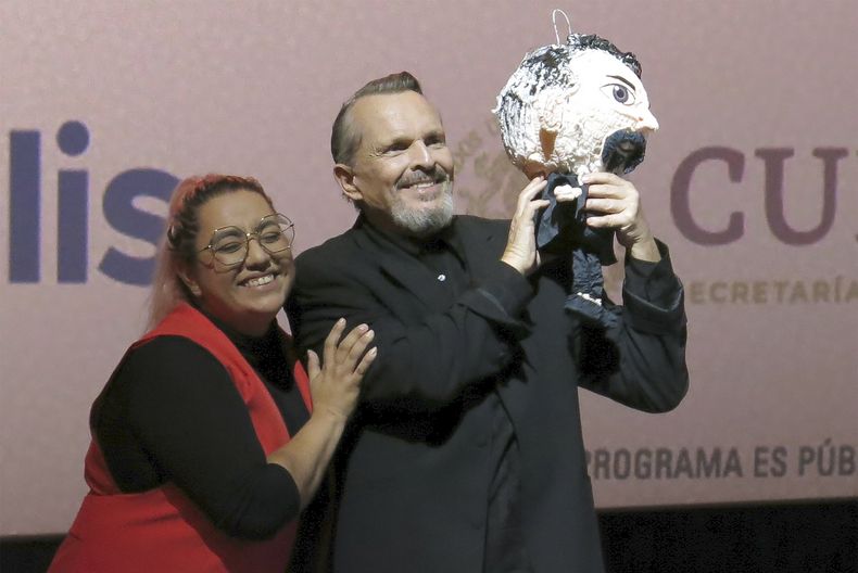 Una fan le regala una piñata al cantante y actor español Miguel Bosé, derecha, durante una charla sobre la película Tacones lejanos en el Festival Internacional de Cine de Morelia en Morelia, México, el lunes 23 de octubre de 2023. (Foto AP/Berenice Bautista)