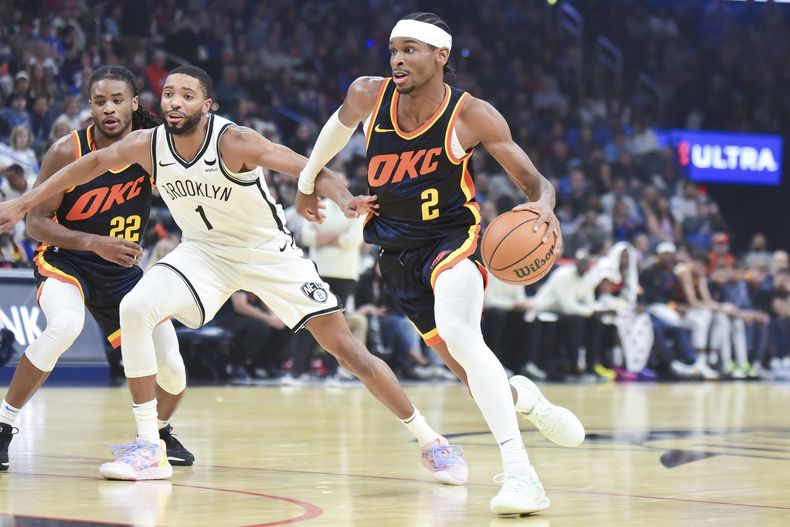 Shai Gilgeous-Alexander (2), del Thunder de Oklahoma City, conduce con el balón rumbo a la canasta, pasando al lado de Mikal Bridges (1), de los Nets de Brooklyn, en el juego de baloncesto de la NBA, el domingo 31 de diciembre de 2023, en Oklahoma City. (AP Foto/Kyle Phillips)