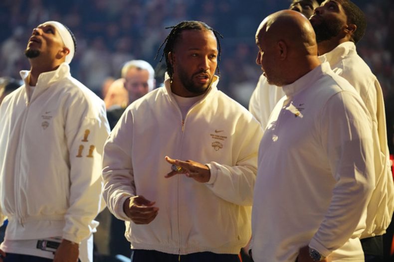 Jalen Brunson, centro, de los Knicks de Nueva York, le muestra a su padre, Rick Brunson, el anillo de campeón de la NBA, previo al partido inaugural de la temporada entre los Knicks de Nueva York y los 76ers de Filadelfia, el martes 20 de octubre de 2026, en Nueva York. (AP Foto/Frank Franklin II)