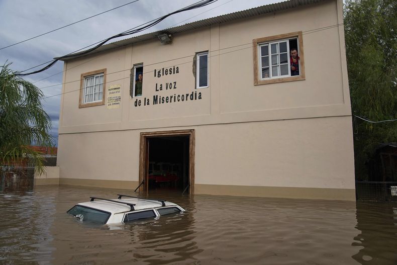 Un vehículo permanece parcialmente sumergido en las aguas de la inundación mientras los residentes observan desde las ventanas de una iglesia, tras las fuertes lluvias en Campana, Argentina, el sábado 17 de mayo de 2025. (Foto AP/Rodrigo Abd)