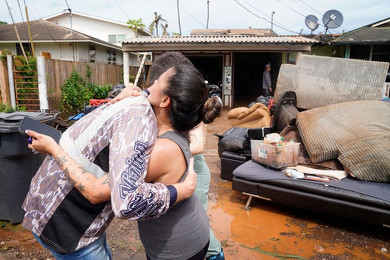 Beau OBrien, voluntario de la iglesia One Love Church de Honolulu, abraza a Sharmaine Arial tras ayudarla a sacar electrodomésticos y muebles dañados por el agua de su casa en Kukea Loop, el domingo 22 de marzo de 2026, en Waialua, Hawai. (Kevin Fujii/Civil Beat vía AP)