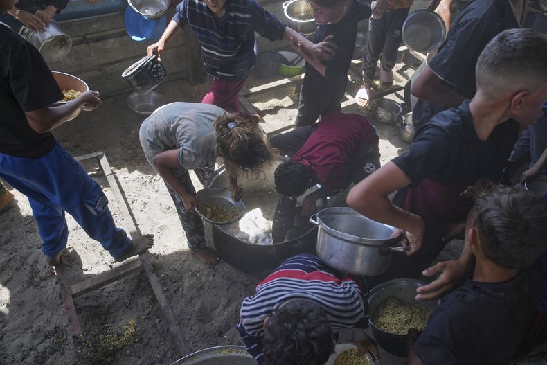 Niños Palestinos rascan una olla de sobras de comida después de que todos los alimentos fueran destruidos en una cocina comunitaria en Jan Yunis, en el sur de la Franja de Gaza, el viernes 9de mayo de 2025.
