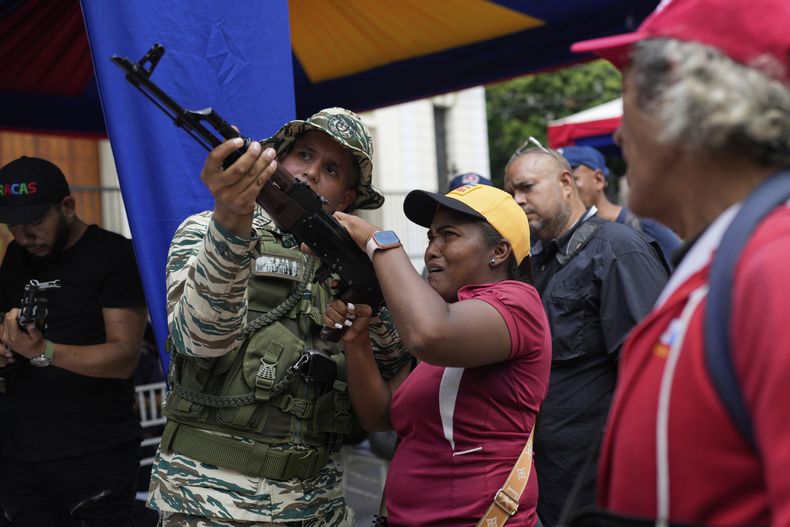 Un miembro de la Milicia Nacional Bolivariana le muestra a una mujer cómo operar un arma durante ejercicios militares en Caracas, Venezuela, el sábado 20 de septiembre de 2025. (Foto AP/Ariana Cubillos)