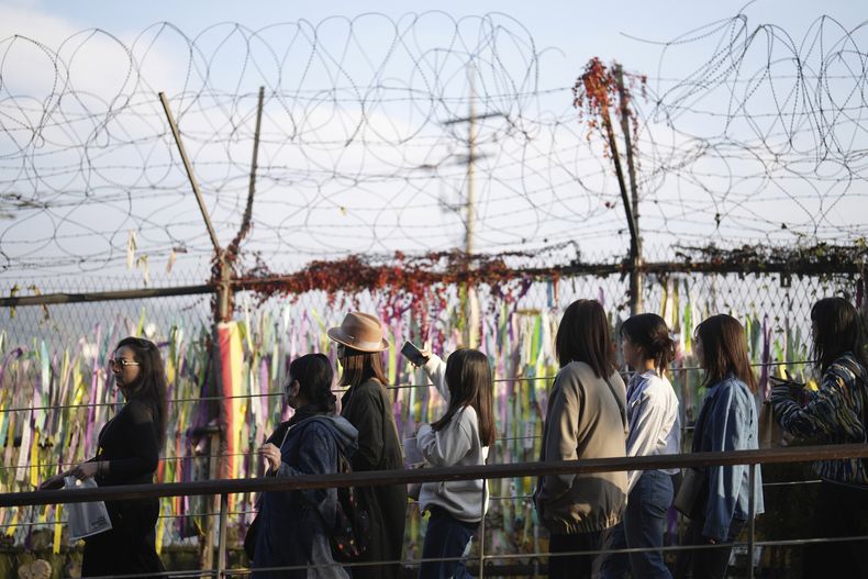 Visitantes caminan cerca de una cerca decorada con lazos con mensajes deseando la reunificación de las dos Coreas en el Pabellón Imjingak en Paju, Corea del Sur, el jueves 31 de octubre de 2024. (AP Foto/Lee Jin-man)