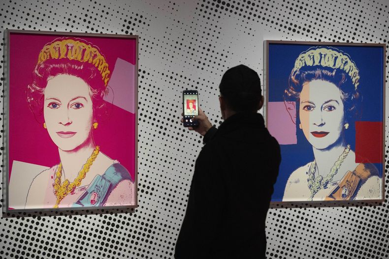 Un hombre toma una foto de una impresión en serigrafía que muestra a la Reina Isabel II, parte de la serie de dieciséis impresiones de cuatro reinas, titulada Reigning Queens, 1985, de Andy Warhol, en el museo Paleis Het Loo en Apeldoorn, Holanda, el miércoles 9 de octubre de 2024, similares a las obras del artista robadas de una galería de Oisterwijk, Holanda, en las primeras horas del viernes 1 de noviembre de 2024. (AP Foto/Peter Dejong)