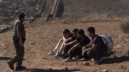 Un agente de la Patrulla Fronteriza pasa junto a cuatro hombres detenidos después de cruzar ilegalmente la frontera México-EEUU, el jueves 23 de enero de 2025, en San Diego. (AP Foto/Gregory Bull)