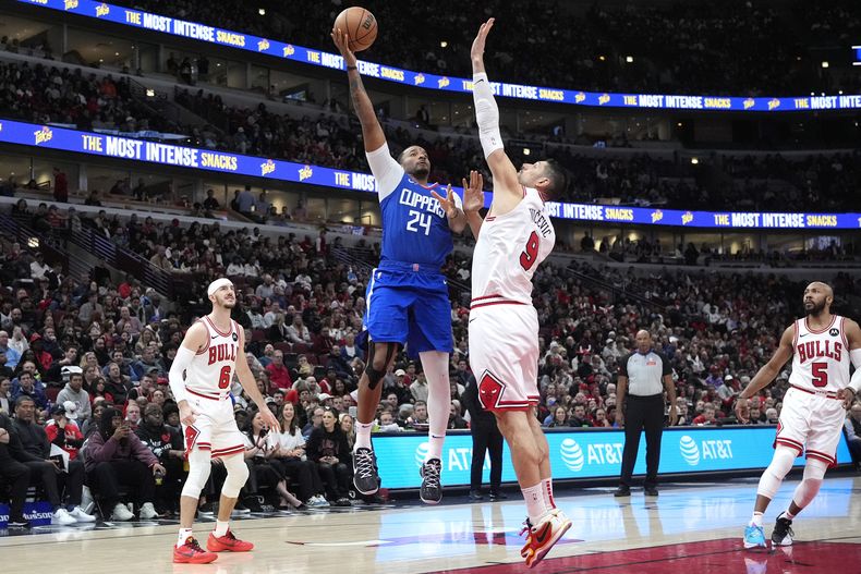 El escolta de los Clippers de Los Ángeles, Norman Powell (24), dispara contra el pívot de los Bulls de Chicago, Nikola Vucevic (9), durante la segunda mitad de un partido de baloncesto de la NBA en Chicago, el jueves 14 de marzo de 2024. (AP Foto/Nam Y. Huh)