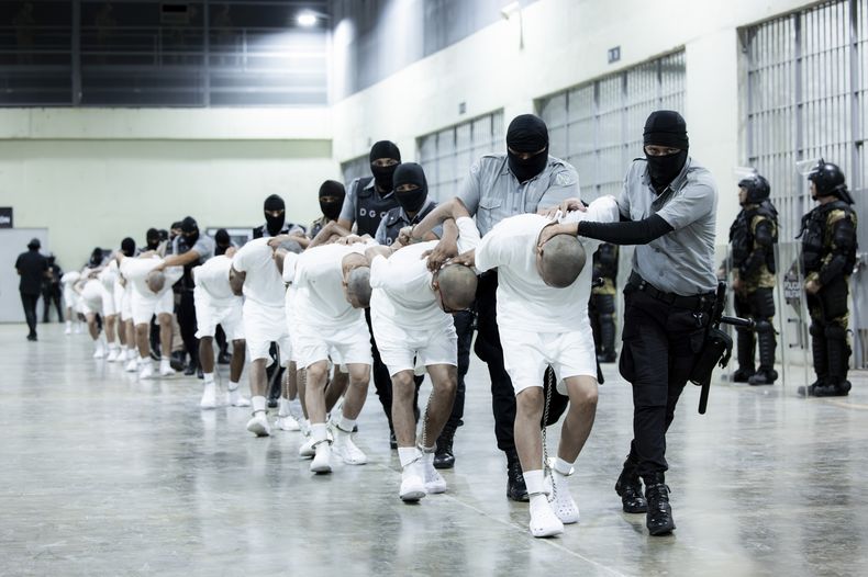 En esta fotografía proporcionada por la oficina de prensa de la presidencia de El Salvador, guardias penitenciarios trasladan a presuntos pandilleros venezolanos, deportados de Estados Unidos, al Centro de Confinamiento del Terrorismo (CECOT) el domingo 16 de marzo de 2025, en Tecoluca, El Salvador. (Oficina de prensa de la presidencia de El Salvador vía AP)