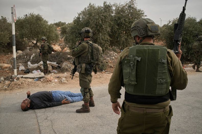 Soldados israelíes, junto a un palestino herido tendido en una carretera, luego de recibir un disparo de soldados israelíes tras el ataque de un colono a palestinos que cosechaban aceitunas en Abu Falah, una localidad en la Cisjordania ocupada, el 16 de octubre de 2026. (AP Foto/Leo Correa)