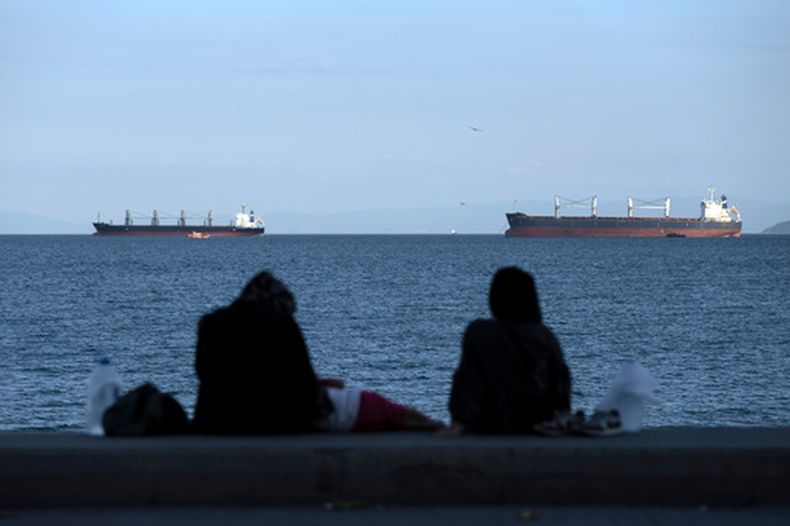 ARCHIVO - Varias personas sentadas frente a buques mercantes anclados en el mar de Mármara a la espera de cruzar el estrecho del Bósfoto en Estambul, Turquía, el 13 de julio de 2022. (AP Foto/Khalil Hamra, archivo)