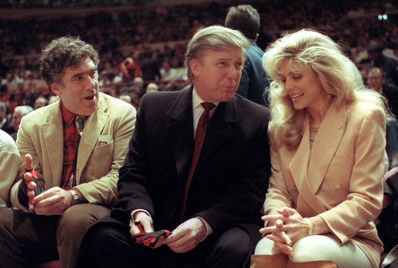 ARCHIVO - Foto del 6 de marzo del 1991, el actor Elliott Gould junto a Donald Trump y su esposa Marla Maples en los asientos de primera fila del juego de los Knicks de Nueva York ante los Suns de Phoenix en el Madison Square Garden. (AP Foto/Steve Freeman, Archivo)
