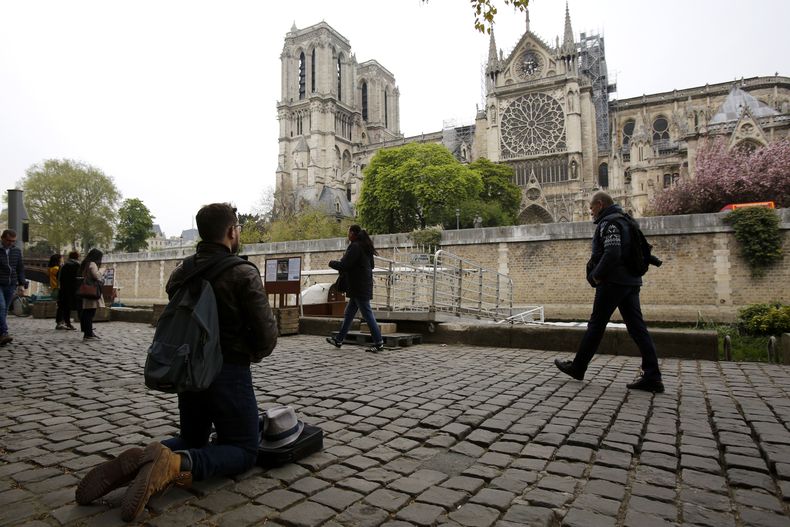 ARCHIVO – Un hombre se arrodilla mientras otras personas acuden a fotografiar la catedral de Notre Dame tras su incendio, en París, el 16 de abril de 2019. (AP Foto/Christophe Ena, Archivo)