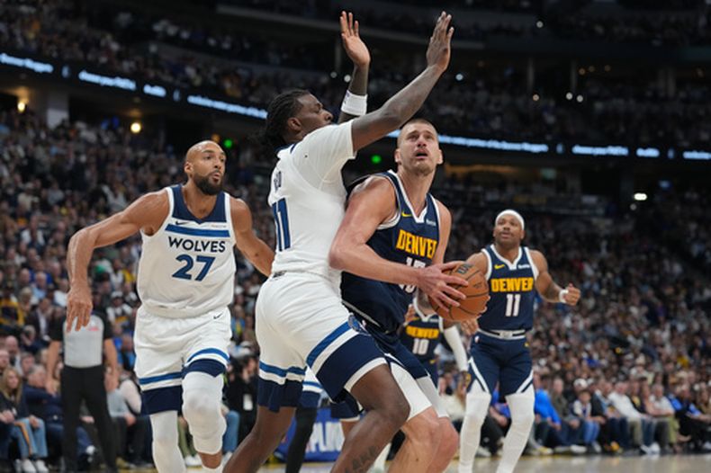 Nikola Jokic, al frente a la derecja, lleva el balón hacia la canasta, mientras Naz Reid, centro izquierda, y Rudy Gobert, izquierda, defienden en la primera mitad del quinto juego de la serie de primera ronda de los playoffs del baloncesto de la NBA, el lunes 27 de abril de 2026, en Denver. (AP Foto/David Zalubowski)