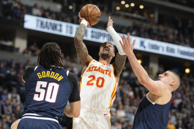 El alero de los Hawks de Atlanta John Collins, al centro, ataca el canasto ante el alero Aaron Gordon y el pívot Nikola Jokic, de los Nuggets de Denver, en la primera mitad del partido del sábado 4 de febrero de 2023, en Denver. (AP Foto/David Zalubowski, Archivo)