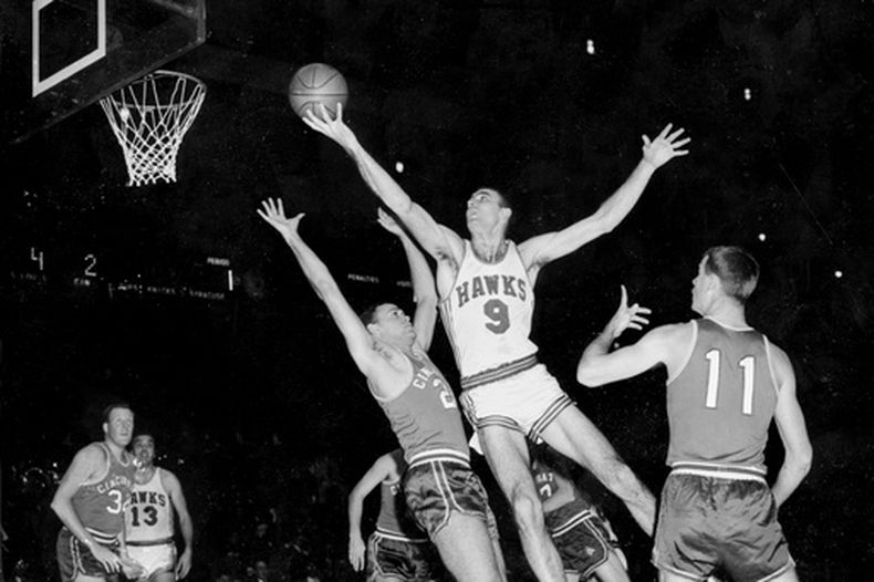 ARCHIVO - En esta foto de archivo del 10 de diciembre de 1957, Bob Pettit, de los Hawks de St. Louis, salta para realizar un disparo a una mano, pero falla en el intento de anotar durante el primer cuarto de un partido de baloncesto de la NBA contra los Royals de Cincinnati en el Madison Square Garden, en la ciudad de Nueva York. Bloqueando a Pettit se encuentra Dick Ricketts (24), de los Royals, mientras Jim Paxson (11) observa la jugada. (Foto AP/Archivo)