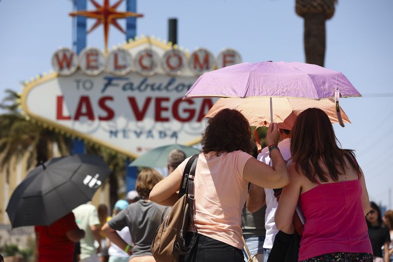 ARCHIVO - Varias personas usan sombrillas para taparse del sol mientras esperan para tomar una foto en el famoso letrero de Bienvenidos a Las Vegas, el 8 de julio de 2024, en Las Vegas. (Wade Vandervort/Las Vegas Sun vía AP)