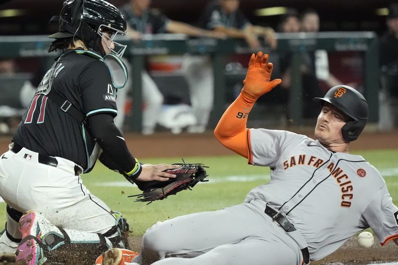 Matt Chapman, derecha, de los Gigantes de San Francisco, se barre para llegar a salvo en el plato para anotar con un jonrón de campo, ante el intento de retirarlo de José Herrera, izquierda, receptor de los Diamondbacks de Arizona, durante la tercera entrada del juego de béisbol el lunes 23 de septiembre de 2024, en Phoenix. (AP Foto/Ross D. Franklin)
