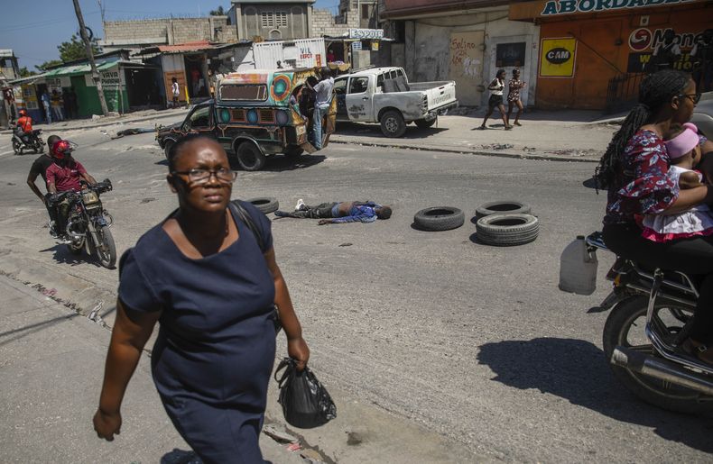 Una mujer camina junto al cuerpo de un hombre, que yace a mitad de una calle de Puerto Príncipe, el jueves 20 de abril de 2023. (AP Foto/Odelyn Joseph)