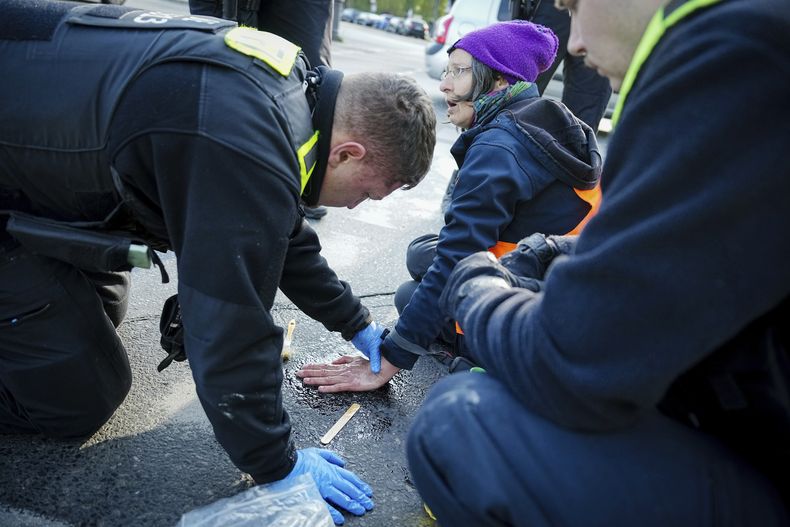 Un agente de policía trata de retirar la mano de una activista que se pegó al asfalto durante una protesta en Grosser Stern, frente a la Columna de la Victoria, en Berlín, el 28 de abril de 2023. (Kay Nietfeld/dpa vía AP)