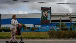 Una mujer pasa en patineta eléctrica frente a una fábrica que exhibe una imagen del fallecido líder cubano Fidel Castro, con la leyenda Socialismo o muerte, en La Habana, Cuba, el jueves 19 de marzo de 2026. (Foto AP/Ramón Espinosa)
