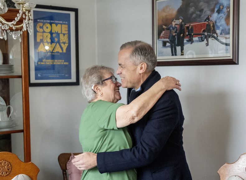 El primer ministro canadiense Mark Carney recibe un abrazo de Beulah Cooper al llegar a la casa de Cooper en Gander, Terranova, Canadá, el 24 de marzo del 2025. (Frank Gunn/The Canadian Press via AP)