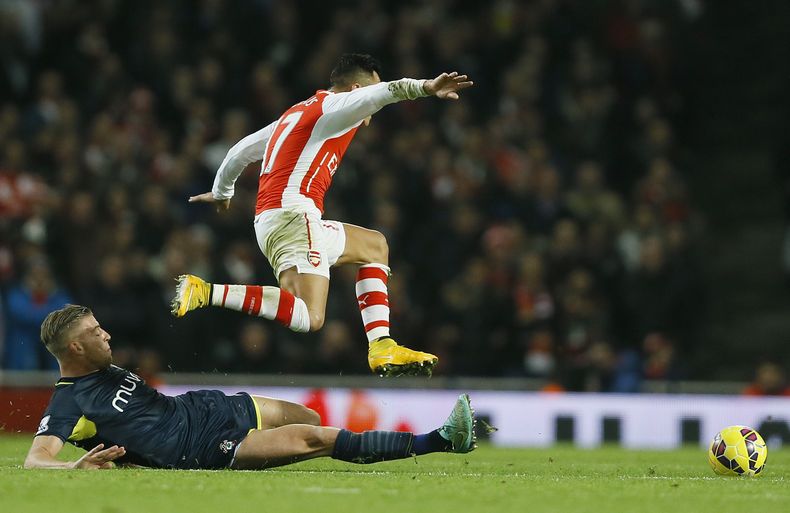 El jugador chileno de Arsenal, Alexis S&aacute;nchez, salta sobre un jugador de Southampton en un partido por la liga Premier el mi&eacute;rcoles, 3 de diciembre de 2014, en Londres. (AP Photo/Kirsty Wigglesworth)