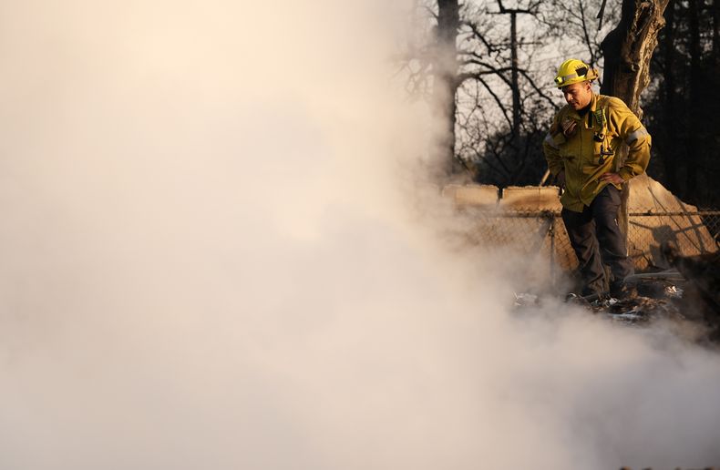 Un bombero, rodeado de humo, se toma un descanso mientras trabaja en la extinción de las brasas en una vivienda destruida por el fuego en Altadena Drive, el 10 de enero de 2025, en Altadena, California. (AP Foto/Chris Pizzello)