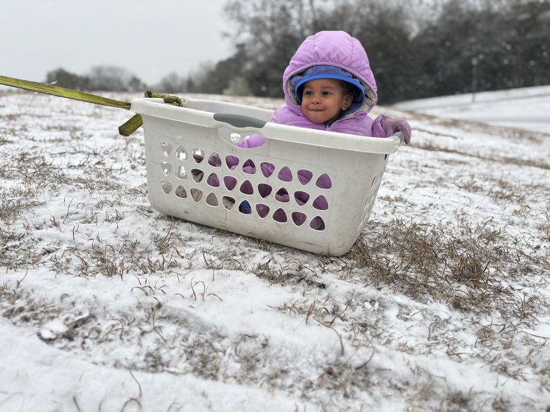 Aria Johnson, de 1 año, juega en la nieve con una cesta como trineo en Montgomery, Alabama, el martes 21 de enero de 2025. (AP Foto/Kim Chandler)
