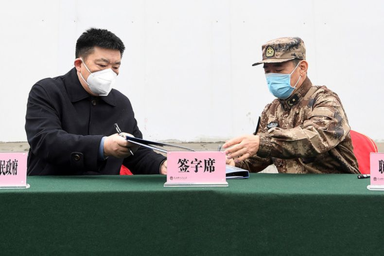Zhou Xianwang, izquierda, alcalde de Wuhan, intercambia documentos con Bai Zhongbin, derecha, subcomandante en jefe de la Fuerza de Apoyo Logístico Conjunto del Ejército Popular de Liberación de China, el 2 de febrero de 2020, durante una ceremonia de entrega en el hospital de campaña temporal de Huoshenshan, en Wuhan, provincia de Hubei, centro de China. (Chinatopix vía AP)