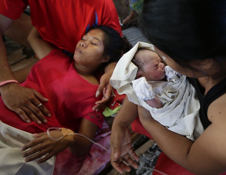 Una personas sostiene a la reci&eacute;n nacida Bea Joy mientras su madre, Emily Ortega, de 21 a&ntilde;os, descansa tras el parto en una cl&iacute;nica improvisada en el aeropuerto de Tacloban el lunes 11 de noviembre de 2013 en Tacloban, provincia de Le