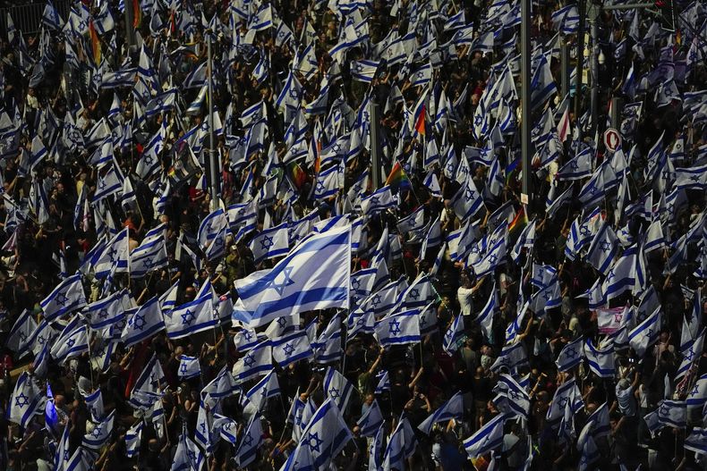 Israelíes agitan banderas de su país durante una protesta en Tel Aviv, el sábado 3 de junio de 2023, contra los planes del primer ministro Benjamin Netanyahu de efectuar cambios en el sistema judicial. (AP Foto/Ariel Schalit)