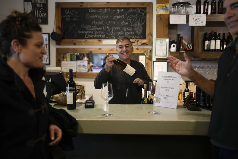 Ofer Bahat vende una botella de vino a Shlomo Benhaim en su bodega Bahat en el kibutz de Ein Zivan, en los Altos del Golán anexionados por Israel, que la mayor parte del mundo considera territorio sirio ocupado, el jueves 19 de diciembre de 2024. (AP foto/Matias Delacroix)