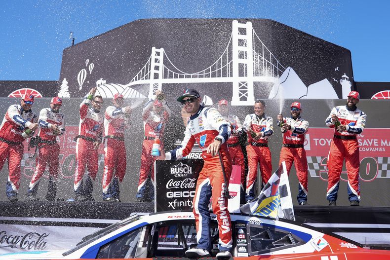 Kyle Larson, centro, es bañado con champaña por sus compañeros de equipo después de ganar la carrera de la NASCAR Cup Series en el Sonoma Raceway, el domingo 9 de junio de 2024, en Sonoma, California. (AP Foto/Godofredo A. Vásquez)