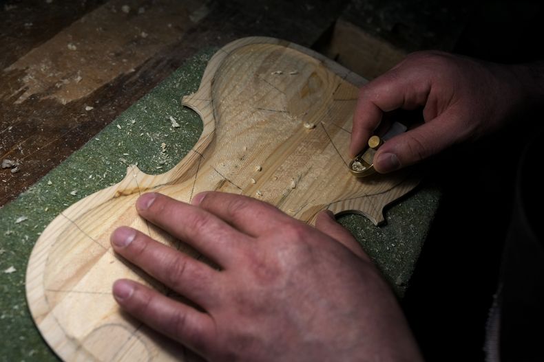 El preso de la cárcel Opera de máxima seguridad Nikolae (quien no proporcionó su apellido) trabaja en un violín hecho con madera de barcos de inmigrantes el viernes 9 de febrero de 2024. Presos de Opera usan la madera para crear instrumentos musicales que la Orquesta del Mar tocó en su debut en el Teatro alla Scala. (Foto AP/Antonio Calanni)