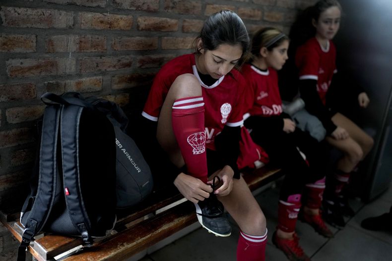 En foto del 19 de junio del 2023, Candelaria Cabrera, jugadora de 12 años del Huracán de Chabas, se ata los zapatos antes del encuentro ante el. Alumni in Arequito, en la provincia de Santa Fe, Argentina. (AP Foto/Natacha Pisarenko)