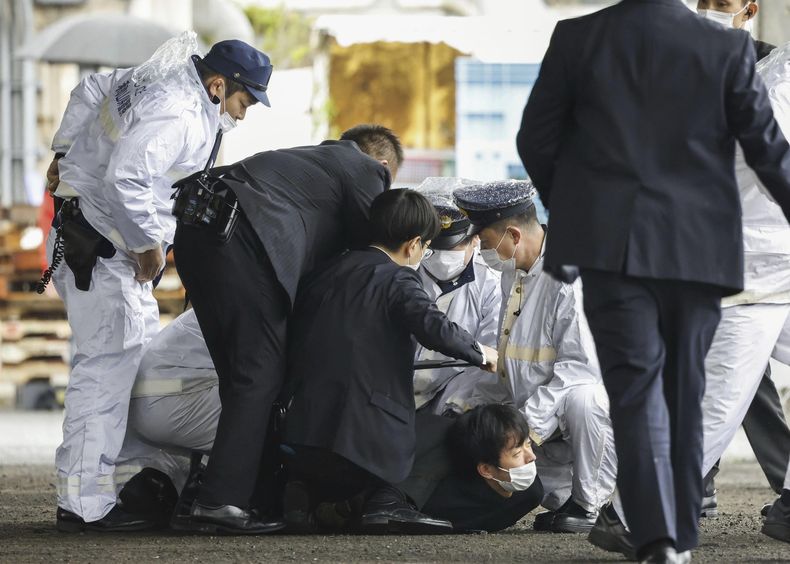Agentes de policía atrapan a un sospechoso (centro, en el piso) luego de que arrojó presuntamente un objeto sospechoso durante la visita del primer ministro, Fumio Kishida, al puerto de Saikazaki para un acto electoral, en Wakayama, en el oeste de Japón, el 15 de abril de 2023. (Kyodo News vía AP, archivo)