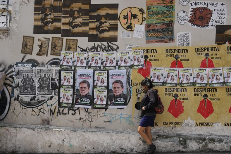 Una mujer camina junto a una pared con carteles de la campaña presidencial en Quito, Ecuador, el miércoles 5 de febrero de 2025. Los ecuatorianos eligen el domingo a un nuevo presidente. (AP Foto/Dolores Ochoa)