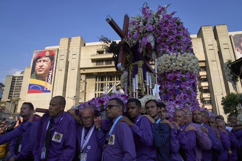 Fieles llevan una carroza con una estatua de Jesucristo, frente a un cartel del fallecido expresidente Hugo Chávez, durante la procesión de Semana Santa del Nazareno de San Pablo en Caracas, Venezuela, el miércoles 16 de abril de 2025. (AP Foto/Ariana Cubillos)