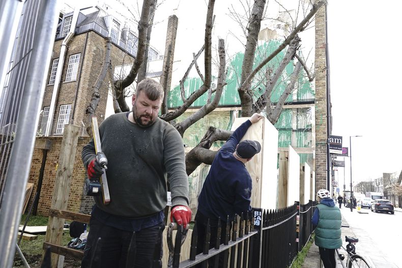 Marcos y protecciones son colocadas junto a la obra de arte de Banksy en el costado de un edificio residencial en Hornsey Road, al norte de Londres, el miércoles 27 de marzo de 2024. La obra que ha sido cubierta con láminas de metacrilato para protección tras un aparente acto de vandalismo. (Aaron Chown/PA vía AP)