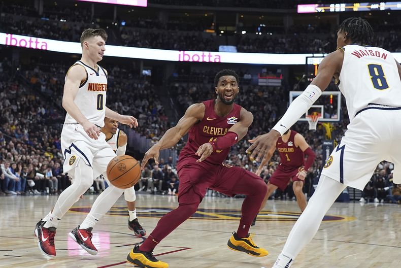 Donovan Mitchell, centro, de los Cavaliers de Cleveland, pasa el balón ante la presión defensiva de Christian Braun, izquierda, y Peyton Watson, de los Nuggets de Denver, en la segunda mitad del juego de baloncesto de la NBA, el viernes 27 de diciembre de 2024, en Denver. (AP Foto/David Zalubowski)