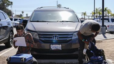 Dos inmigrantes revisan su equipaje en un estacionamiento tras ser detenidos por las autoridades estadounidenses y procesados para ver si se les concede asilo, el martes 7 de mayo de 2024, en San Diego. (AP Foto/Ryan Sun)